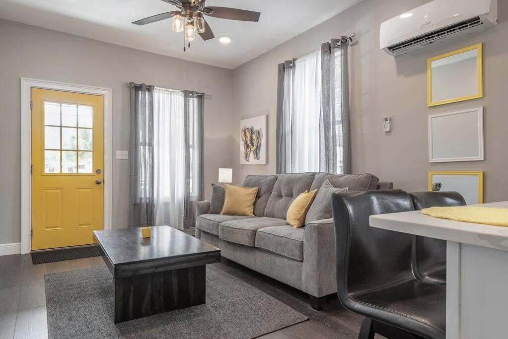 a living room with a gray couch and a yellow door at Gambino Getaway Shotgun style apt in the heart of Ybor City in Tampa