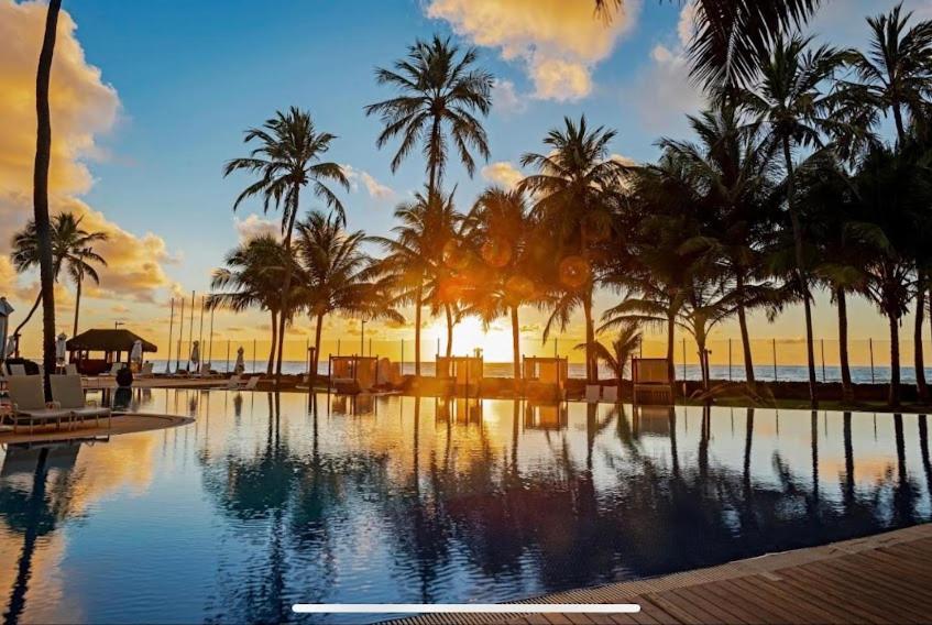 una piscina con palmeras y puesta de sol en Flat no Hotel Jatiúca suítes resort en Maceió