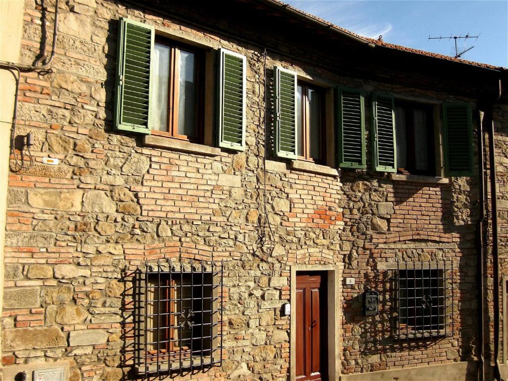 un ancien bâtiment en briques avec des fenêtres vertes et une porte dans l'établissement Casa del Ponte, à Lucolena in Chianti