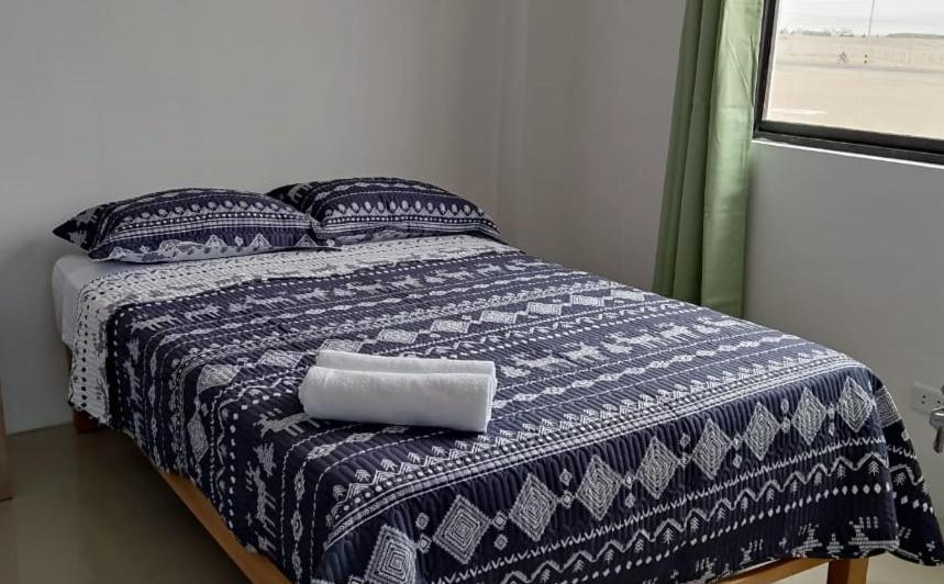 a bed with a blue and white blanket and a window at Urpi Hotel in Paracas