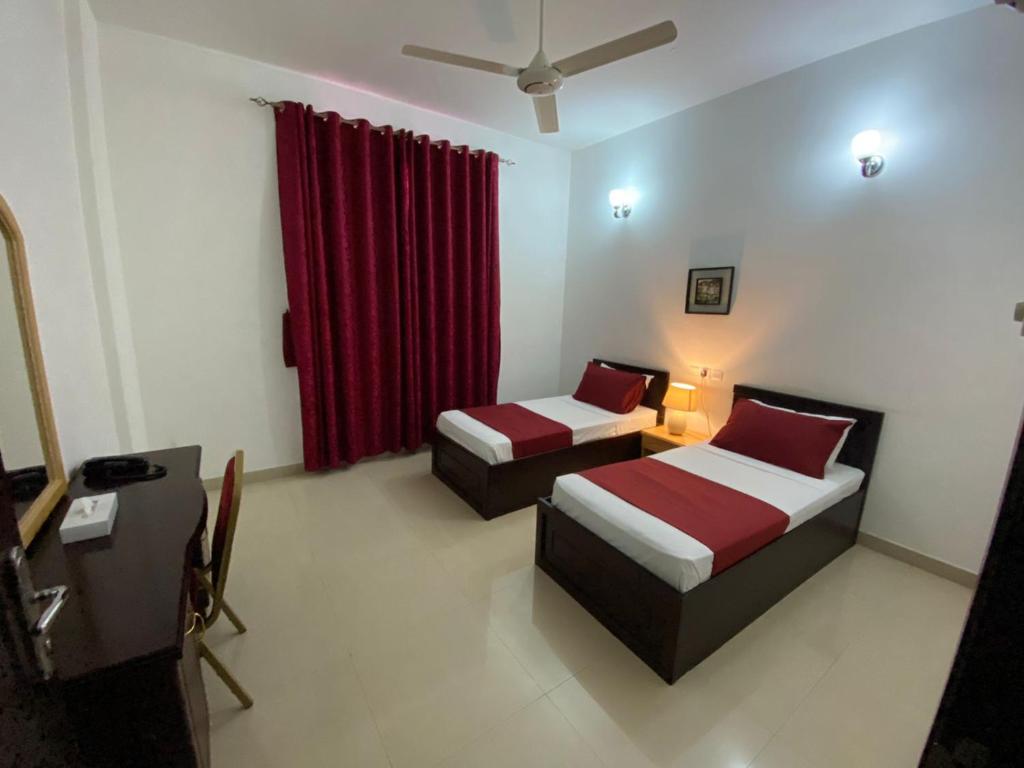 a bedroom with two beds and a red curtain at Azaiba Hotel Apartments in Muscat
