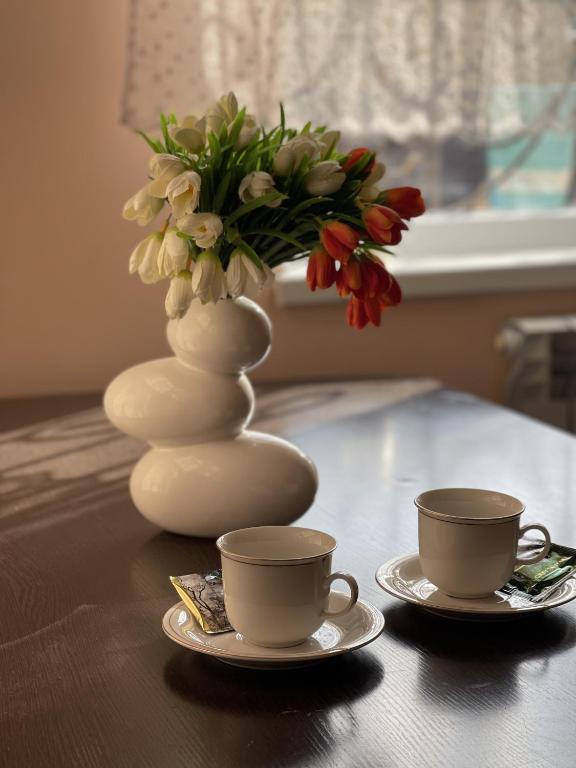 stół z dwoma kubkami i wazon z kwiatami w obiekcie Mondial apartments w mieście Szymkent