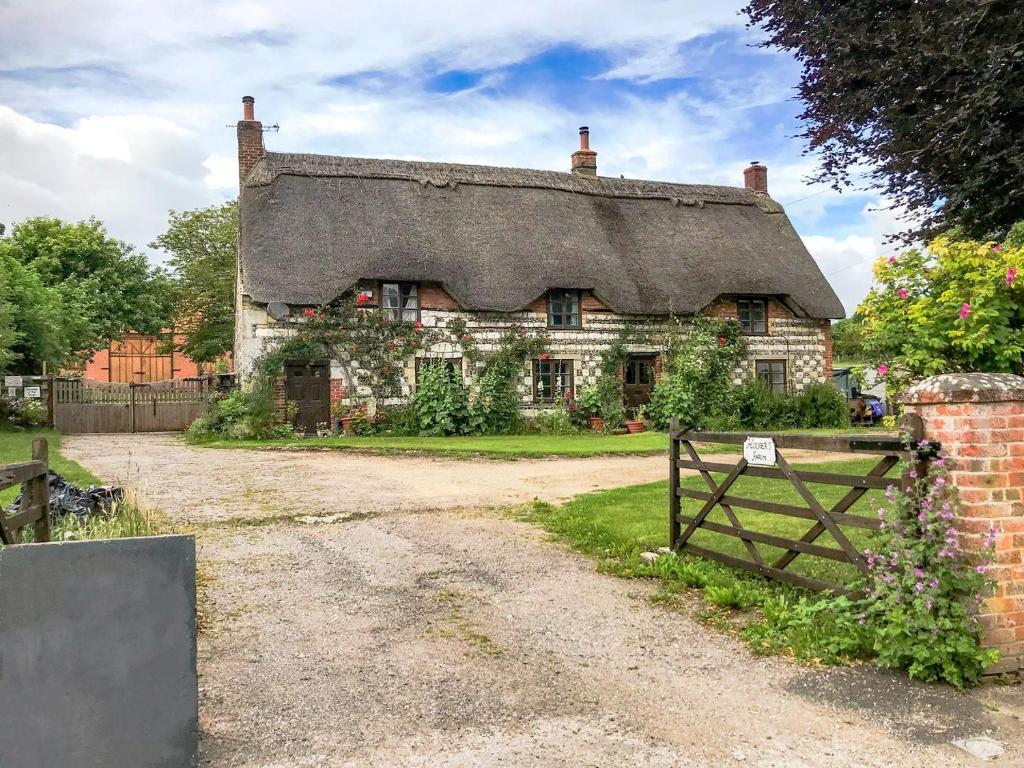 an old stone house with a thatched roof and a gate at Hoopers Farmhouse in Tilshead