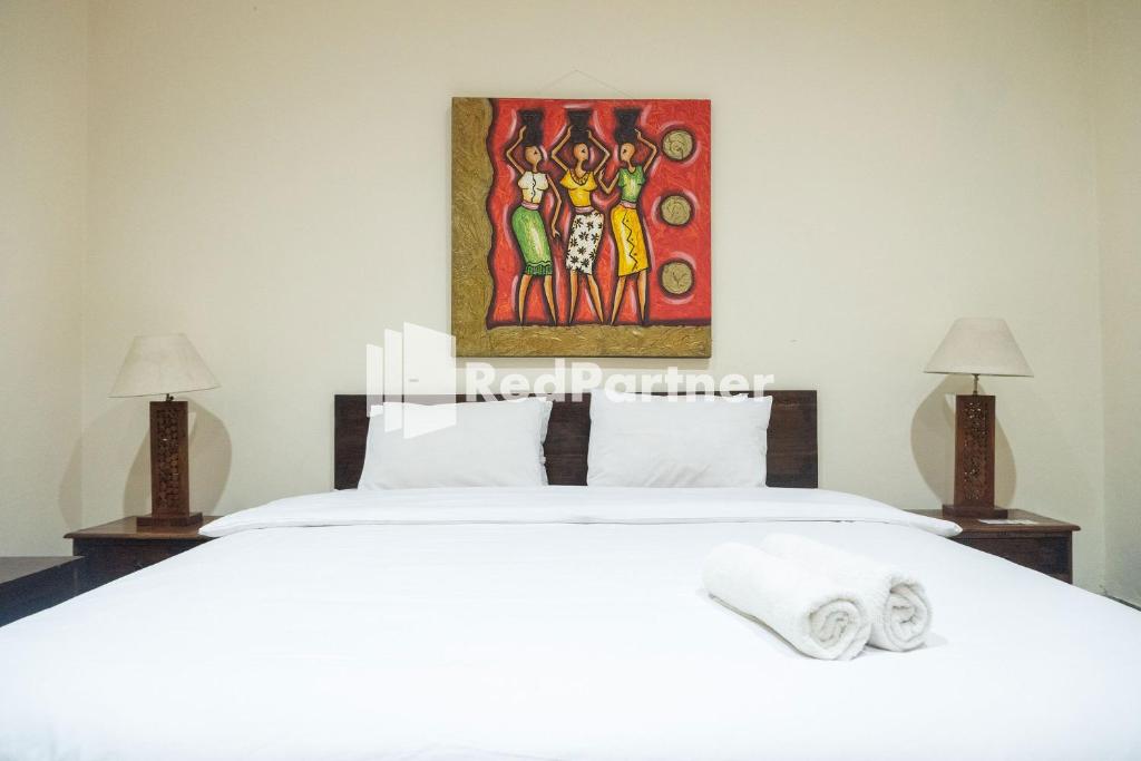 ジョグジャカルタにあるMonginsidi Guest House Syariah Malioboro Yogyakarta Mitra RedDoorzの白いベッドと壁に絵画が飾られたベッドルーム1室