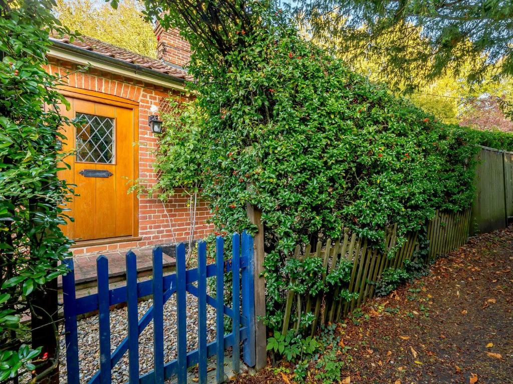 a blue fence in front of a brick house with a door at Manor Cottage Bungalow in Wetheringsett