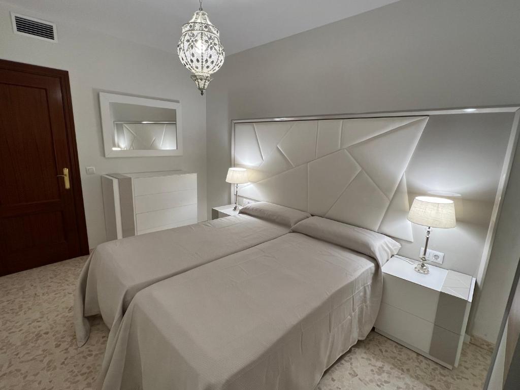 um quarto branco com uma cama grande e um lustre em APARTAMENTO AREVALO LUCENA CENTER em Lucena