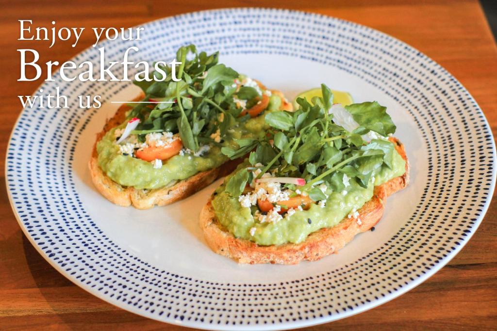 two pieces of bread with avocado and greens on a plate at Grandmas Plus Hotel Seminyak in Seminyak
