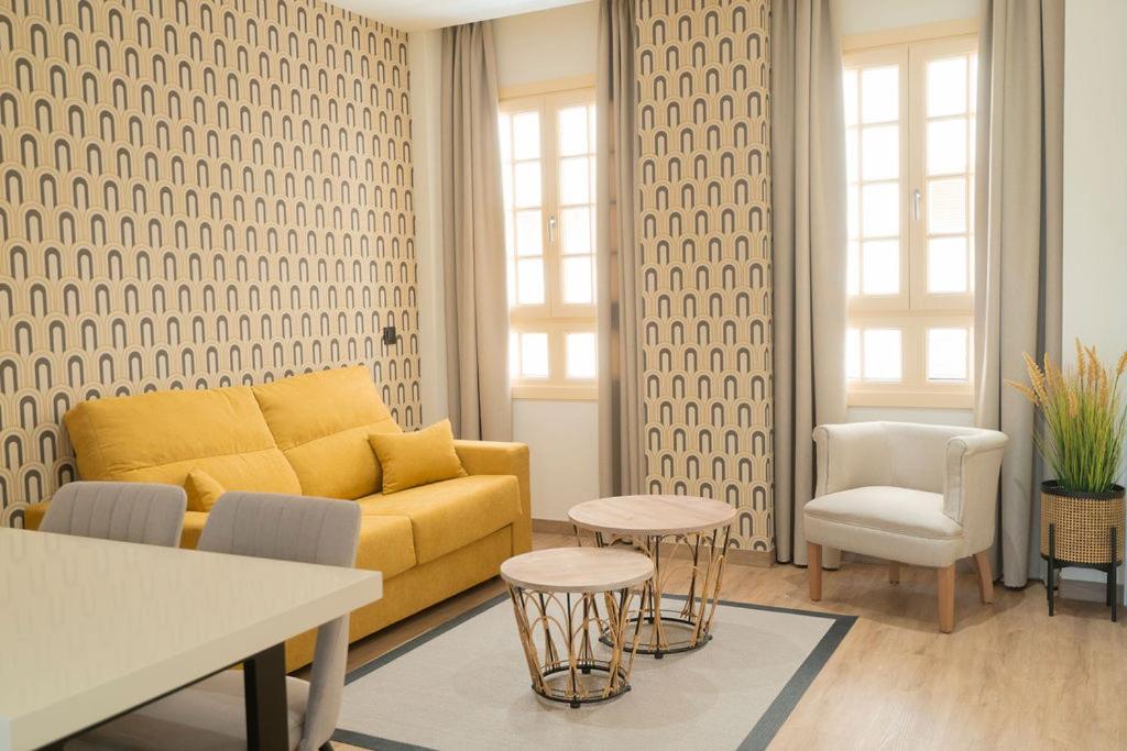 sala de estar con sofá amarillo y sillas en Suites Chinitas, en Málaga