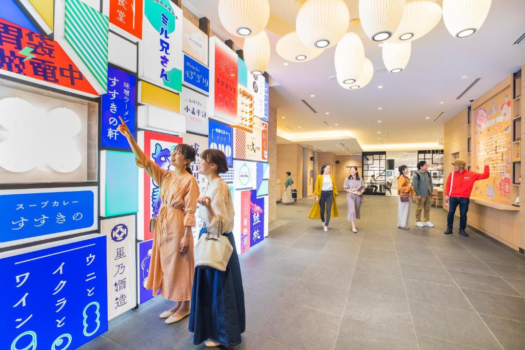 zwei Frauen stehen in einem Einkaufszentrum und zeigen auf Schilder an der Wand. in der Unterkunft OMO3 Sapporo Susukino by Hoshino Resorts in Sapporo