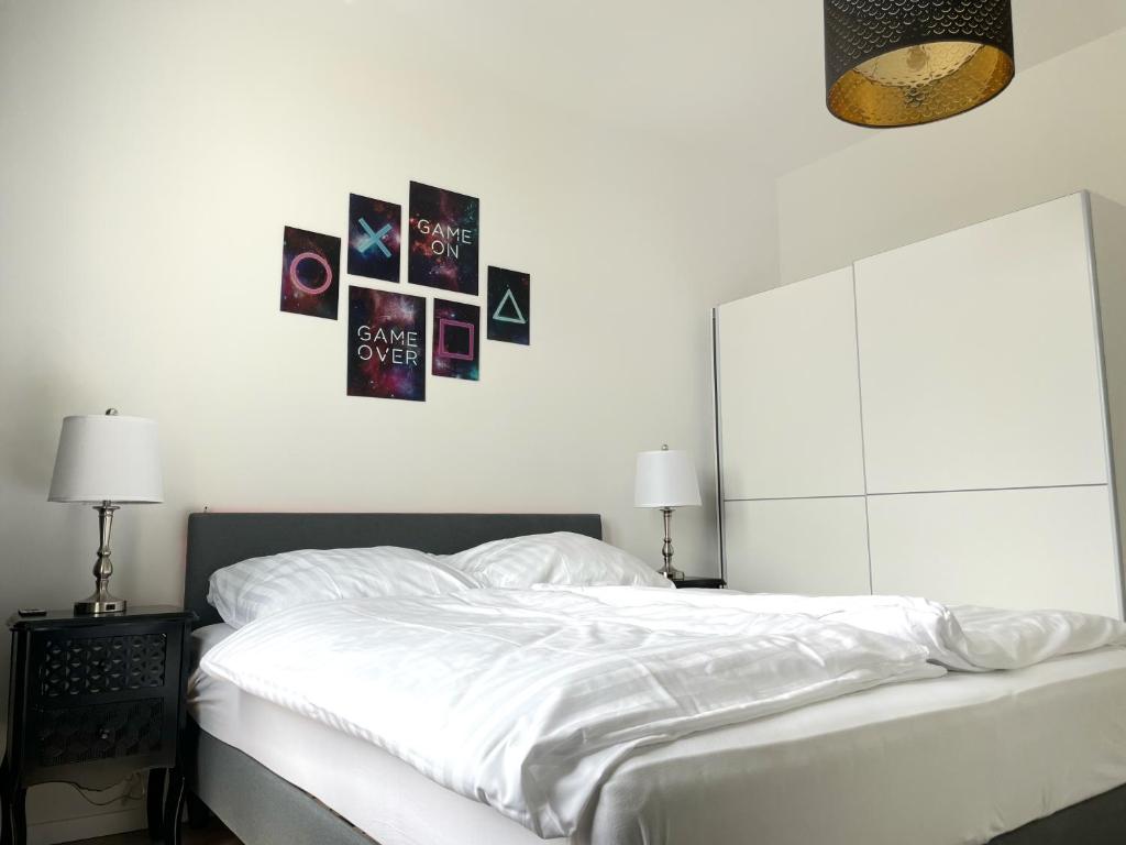 ein Schlafzimmer mit einem weißen Bett mit Bildern an der Wand in der Unterkunft Gaming PS5 + 65 Zoll 4K TV Wohnung mit Balkon in Dortmund