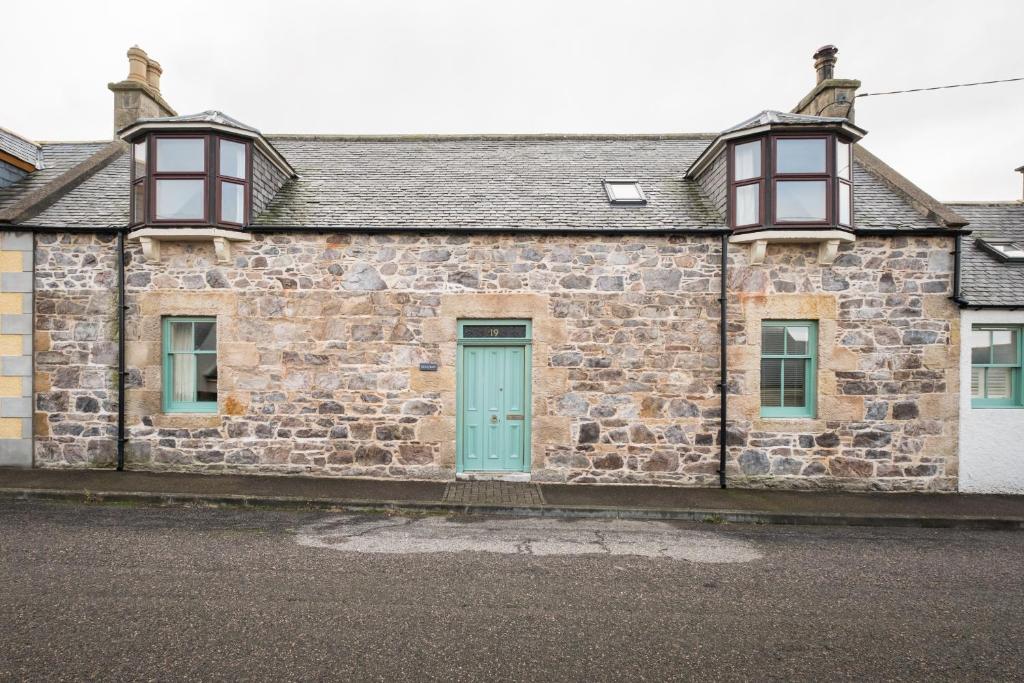 an old stone building with a green door and windows at Seaside cottage on Moray coast in Portknockie