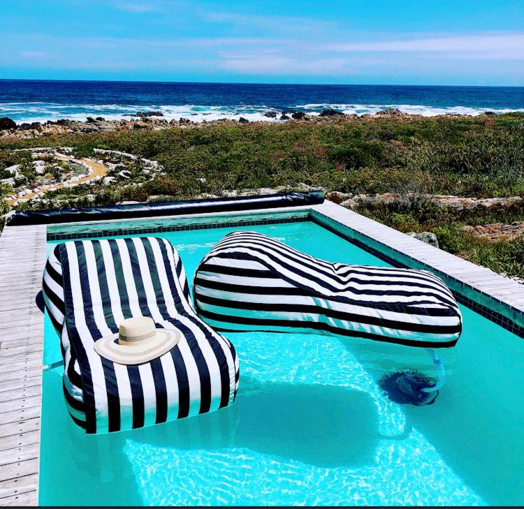 a swimming pool with two lounge chairs and the beach at Kalliste an exclusive retreat in Bettyʼs Bay