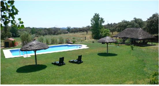 Zalamea la Real的住宿－Cortijo Zalamea，两把遮阳伞和椅子放在靠近游泳池的草地上