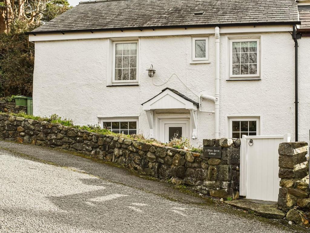 a white house with a stone fence in front of it at 2 White Horses Cottages in Pwllheli