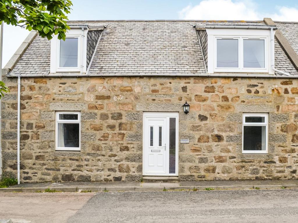 a stone house with a white door and windows at Forvie View in Collieston