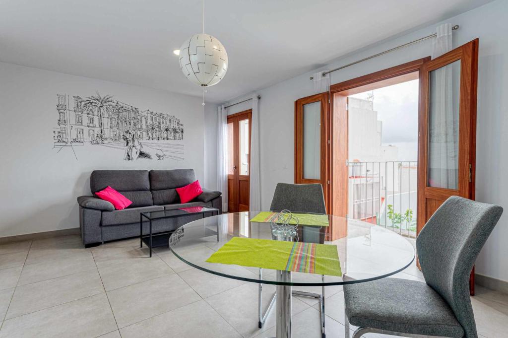 Vegueta Luxury Apartments في لاس بالماس دي غران كاناريا: غرفة معيشة مع طاولة وكراسي زجاجية