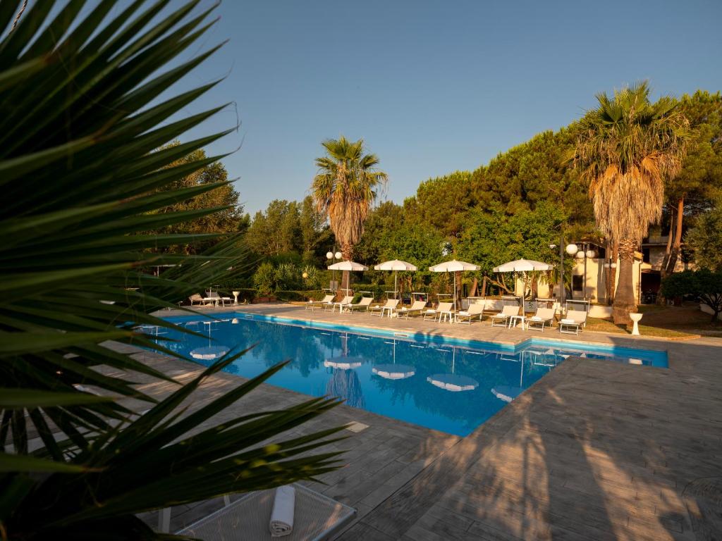 a swimming pool with umbrellas and chairs and trees at Santamaria Village Resort Ascea in Ascea