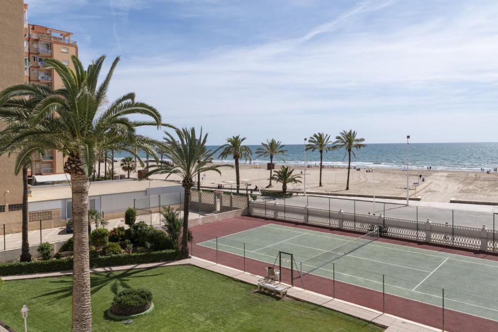 a tennis court with palm trees and the beach at Lider, 2-G in Cullera