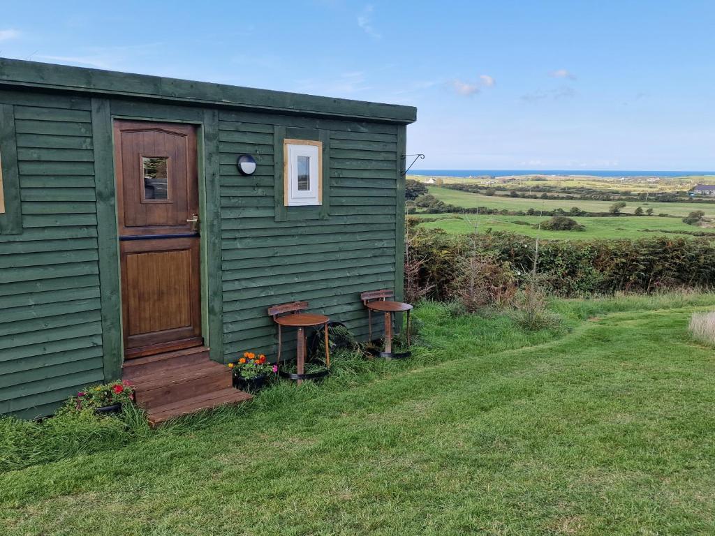 a green shed with two benches and a door at Stunning 1-Bed shepherd hut in Holyhead in Holyhead