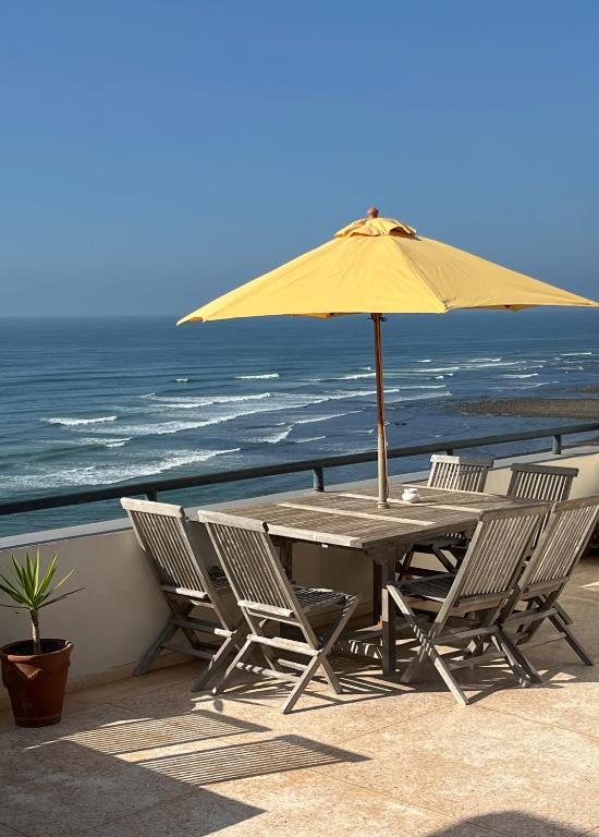 a table and chairs with an umbrella and the ocean at logis la marine in Sidi Ifni
