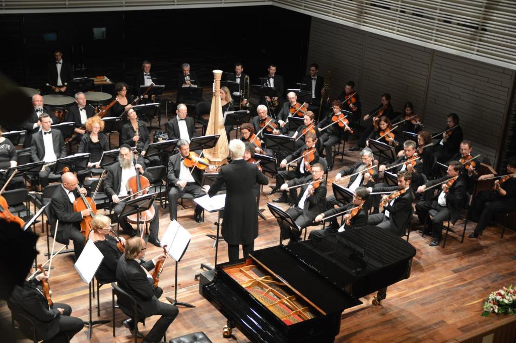 an orchestra performing in front of a crowd of people at Elma Hotel and Art Complex in Zikhron Ya'akov