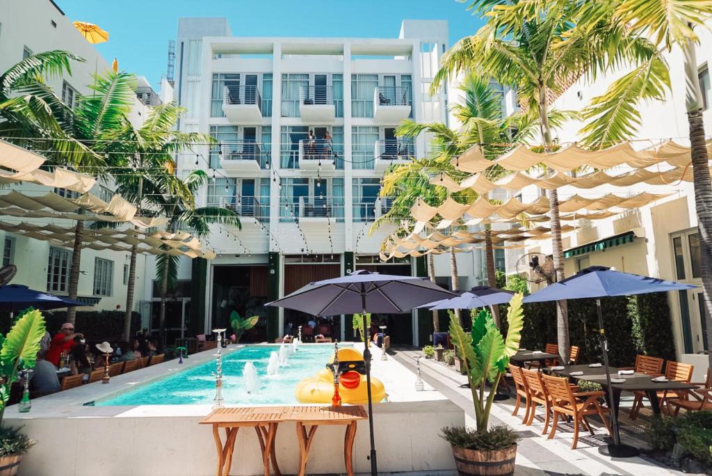 una piscina con mesas y sombrillas junto a un edificio en The Fairwind Hotel en Miami Beach