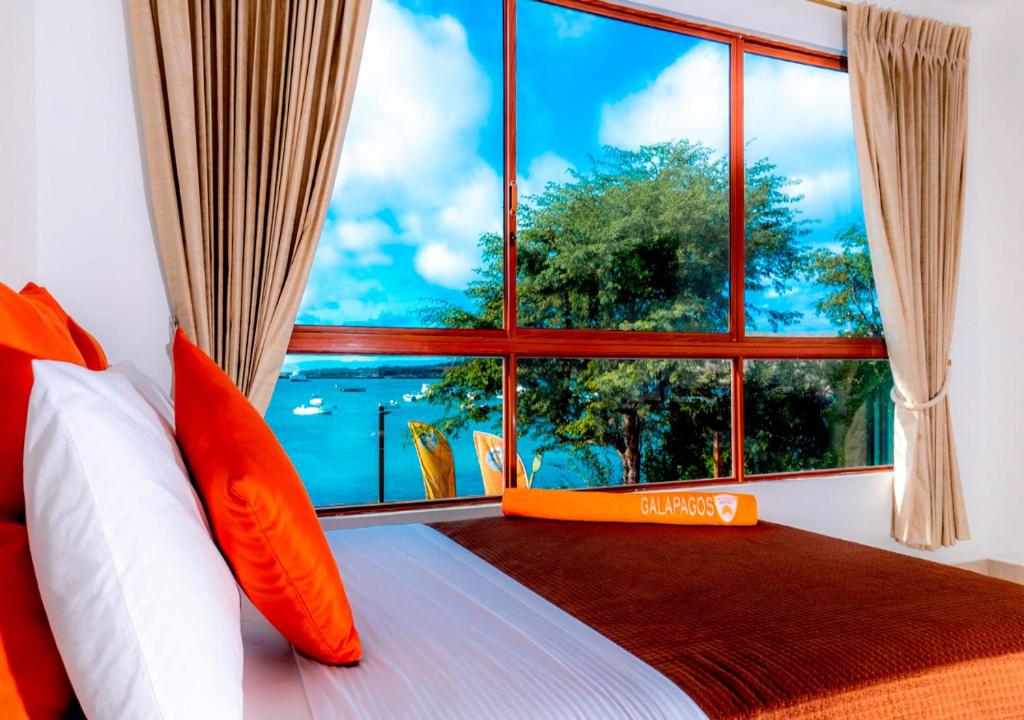 Schlafzimmer mit einem großen Fenster und einem Bett mit orangefarbenen Kissen in der Unterkunft La Zayapa Hotel in Puerto Baquerizo Moreno