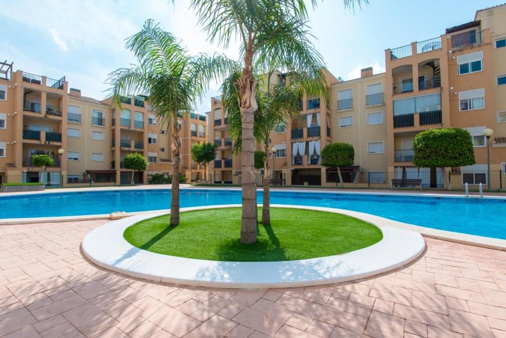 a pool with two palm trees in front of a building at Altorreal Más que apartamentos in Murcia