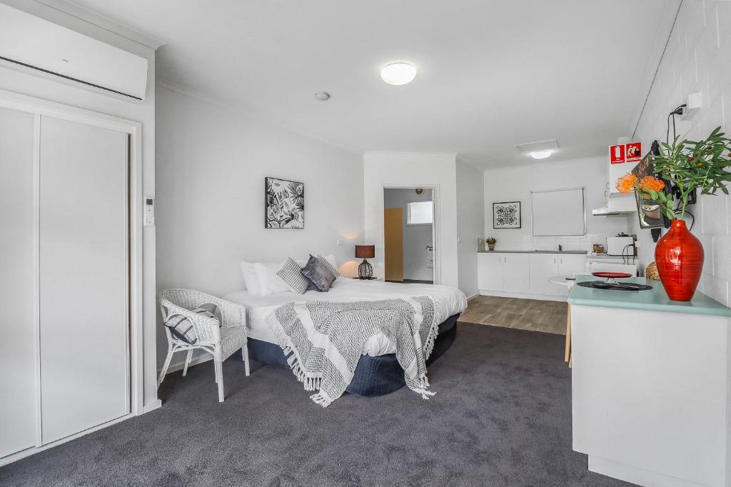 a white bedroom with a bed and a chair at Mibnb Geelong CBD Spacious Studio Apartments in Geelong