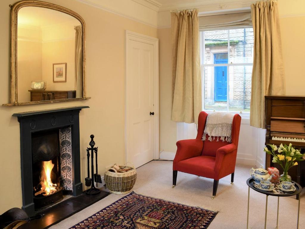 a living room with a fireplace and a red chair at Sanderling End in Lowick