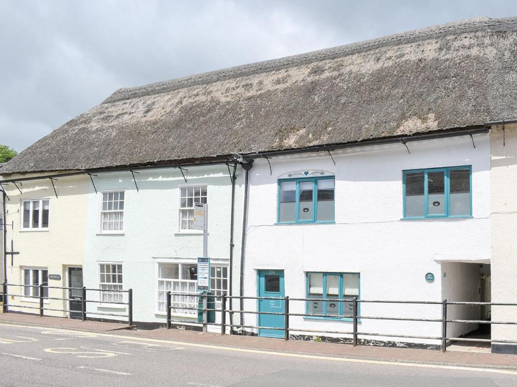 a white building with blue windows and a thatched roof at Teal Cottage in Honiton