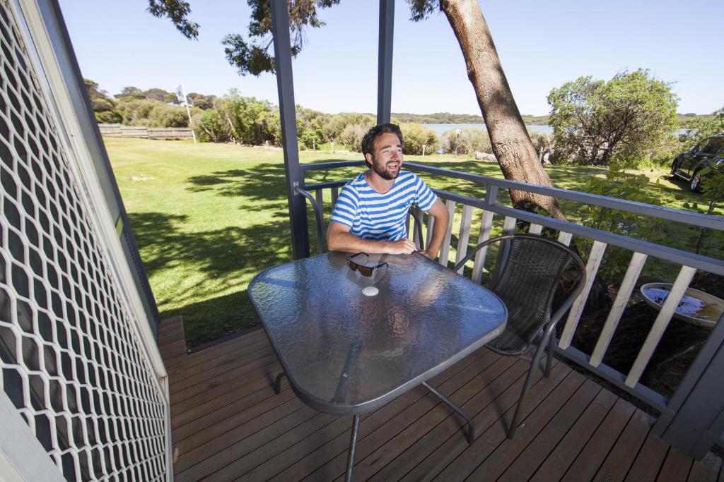 a man sitting at a table on a deck at Lakeside Tourist Park in Robe