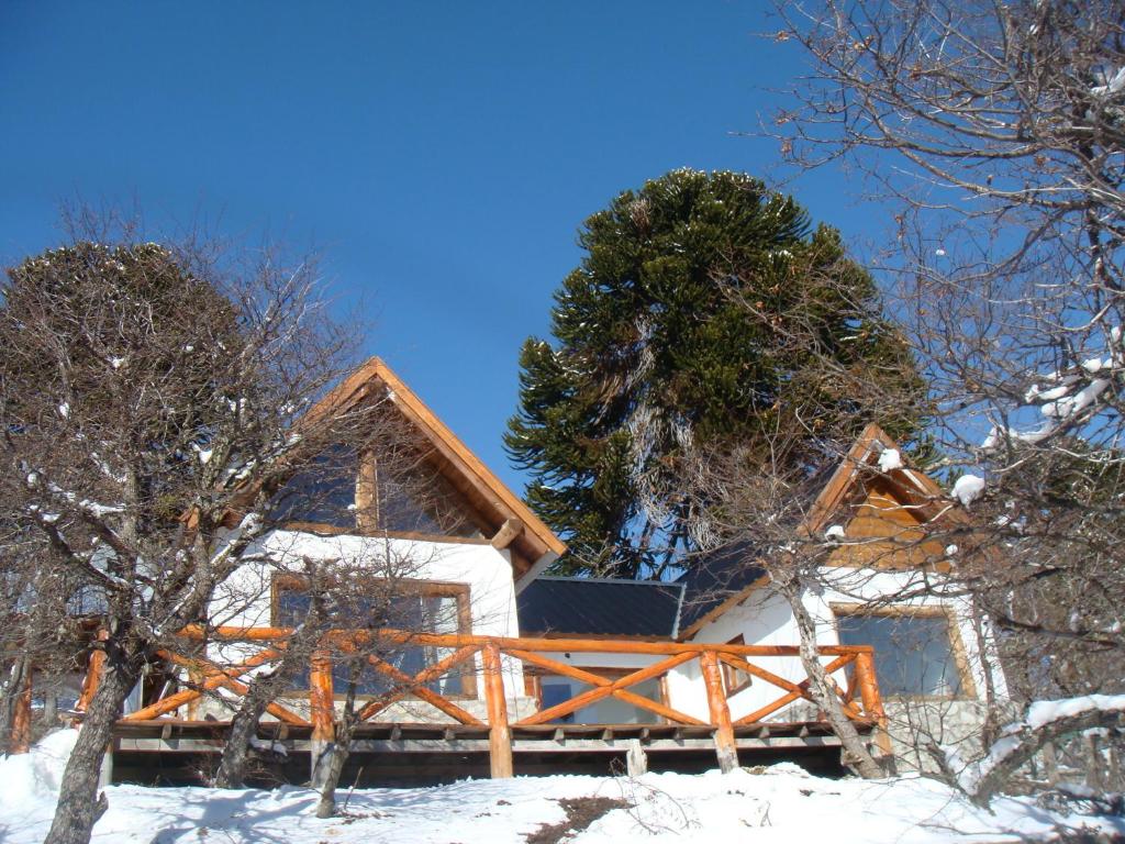 una cabaña de madera en la nieve con un árbol en Cabañas Altos de Moquehue in 