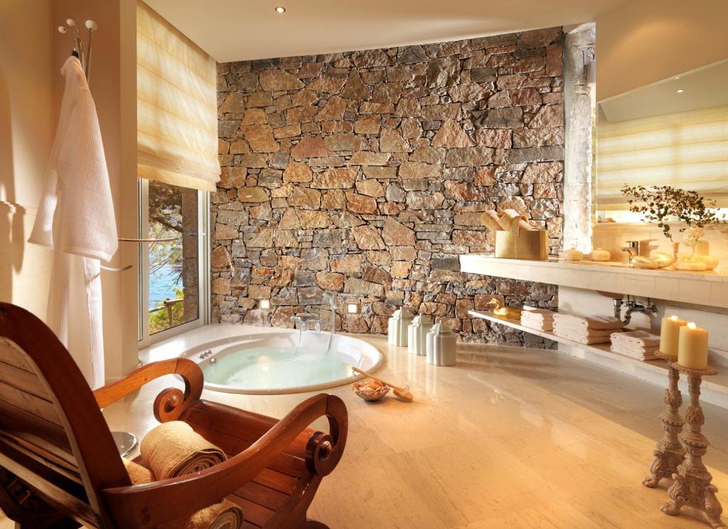 a bathroom with a tub and a stone wall at Out Of The Blue Resort & Spa in Agia Pelagia