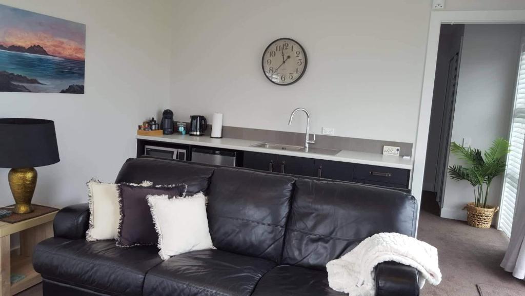 a black leather couch in a living room with a clock on the wall at Waterways Escape in Whitianga