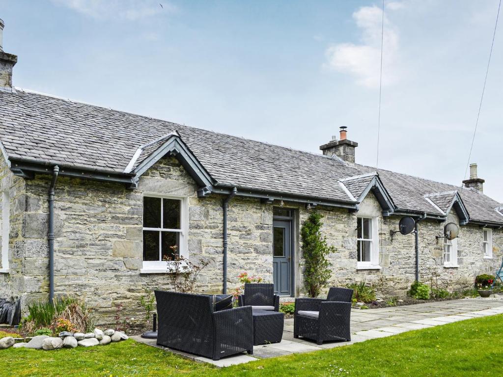 une maison en pierre avec des chaises noires devant elle dans l'établissement Riverside Cottage, à Blair Atholl