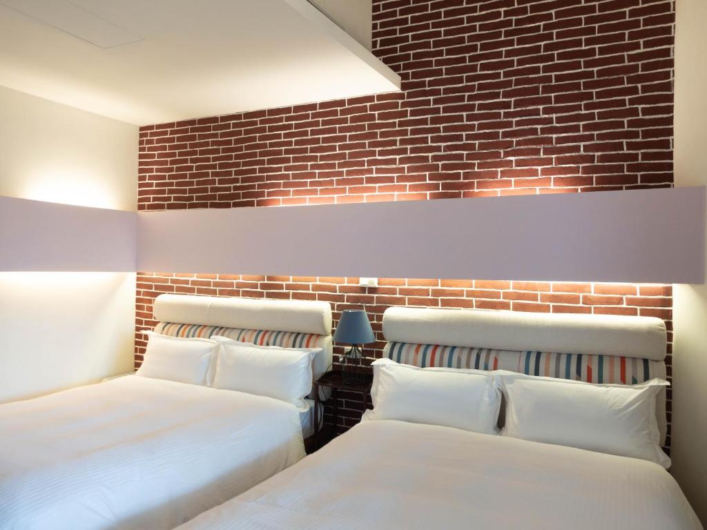 - 2 lits dans une chambre avec un mur en briques dans l'établissement Jiufen Breeze 九份惠風民宿ｌ6人包棟小屋, à Jiufen