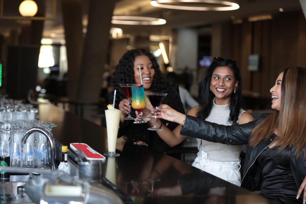 three women sitting at a bar holding drinks at The Capital on the Park in Johannesburg