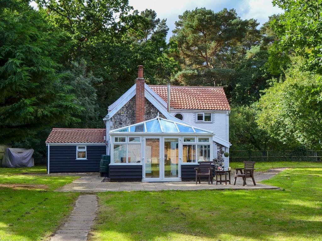 Tree Tops Cottage في Mundford: منزل صغير مع حديقة شتوية في الفناء