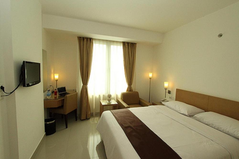 a bedroom with a bed and a desk and a window at Triniti Hotel Jakarta in Jakarta