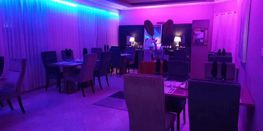 une salle à manger avec éclairage violet, tables et chaises dans l'établissement L'Address Bar-Piscine-Restaurant, à Cotonou