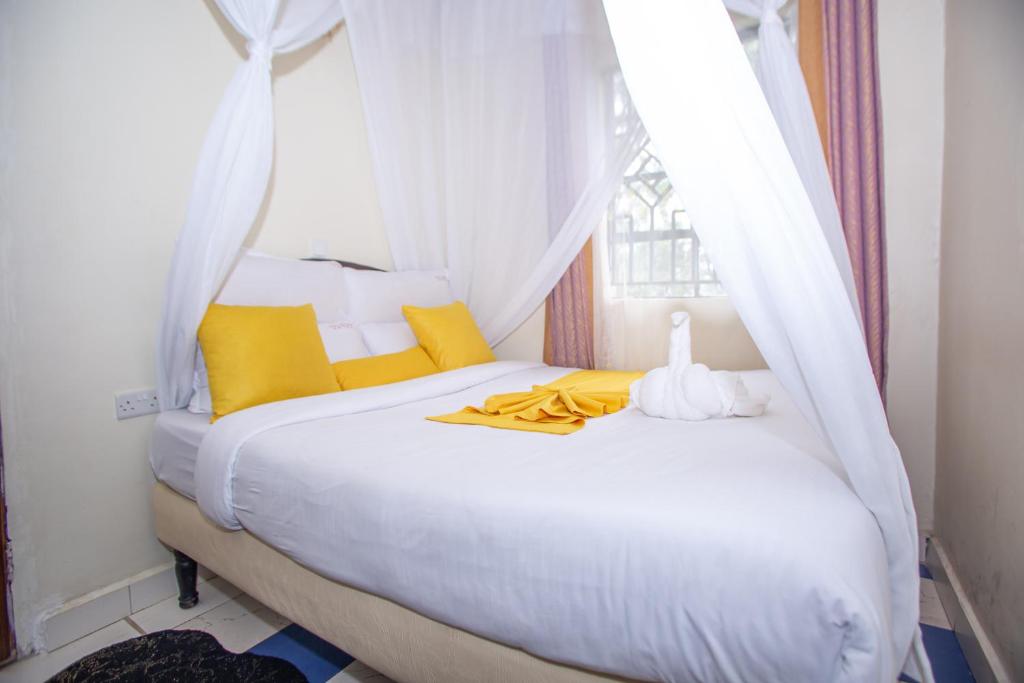 Cama blanca con almohadas amarillas y ventana en Happy Springs Hotel & Accomodation, en Kericho