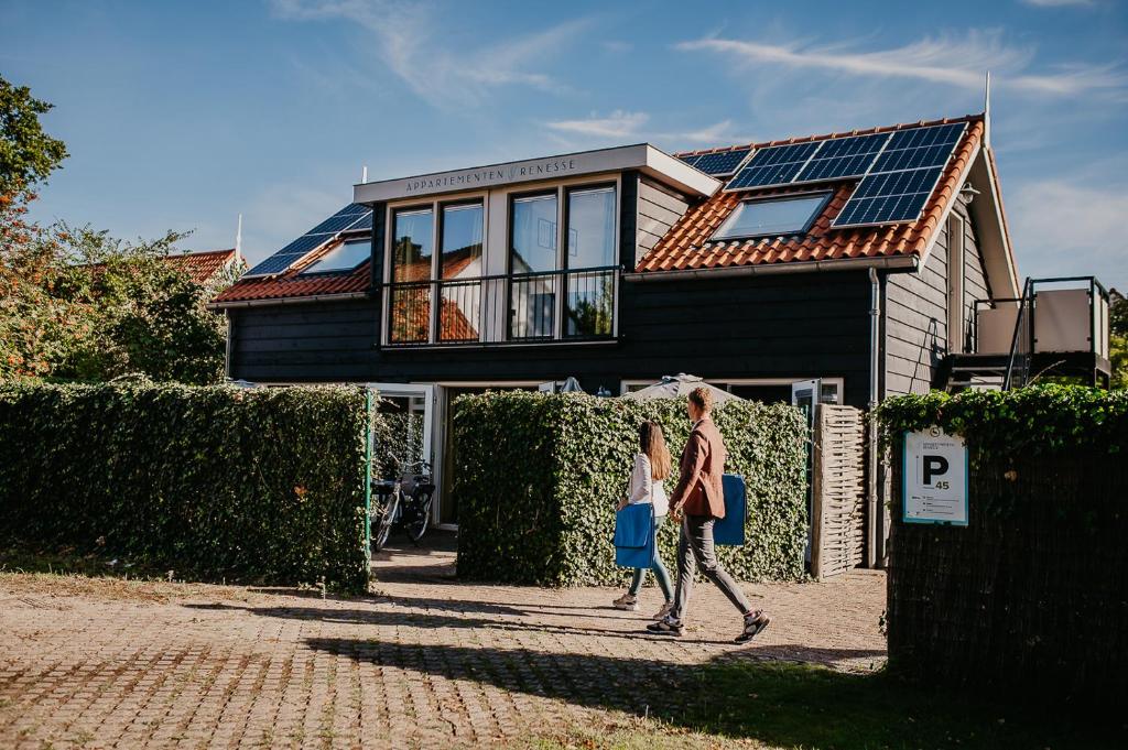 レネッセにあるAppartementen Renesseの太陽電池パネルを持つ家の前を歩く二人