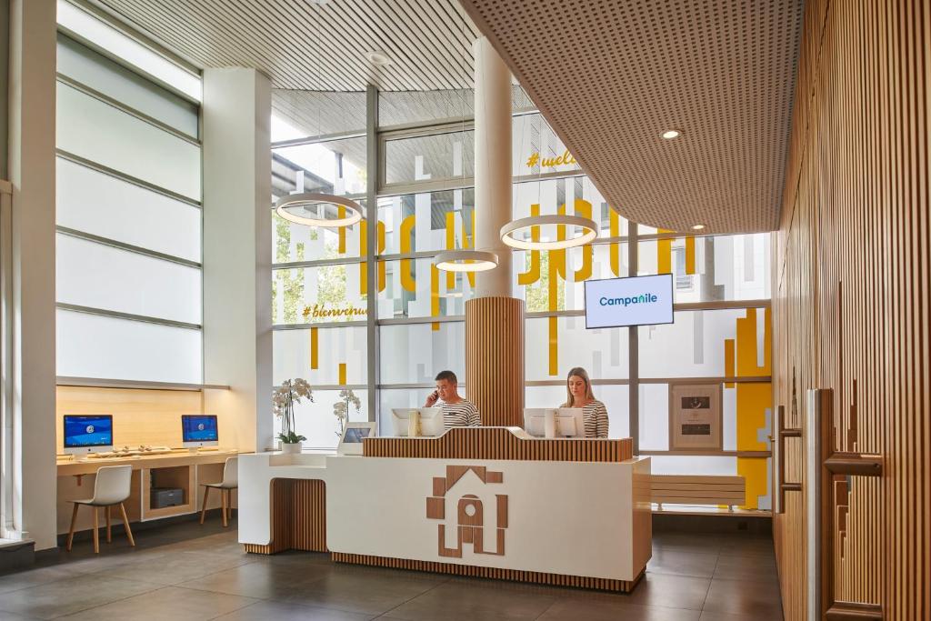 - un hall avec deux personnes assises à un bureau dans un bâtiment dans l'établissement CAMPANILE PARIS 12 - Bercy Village, à Paris
