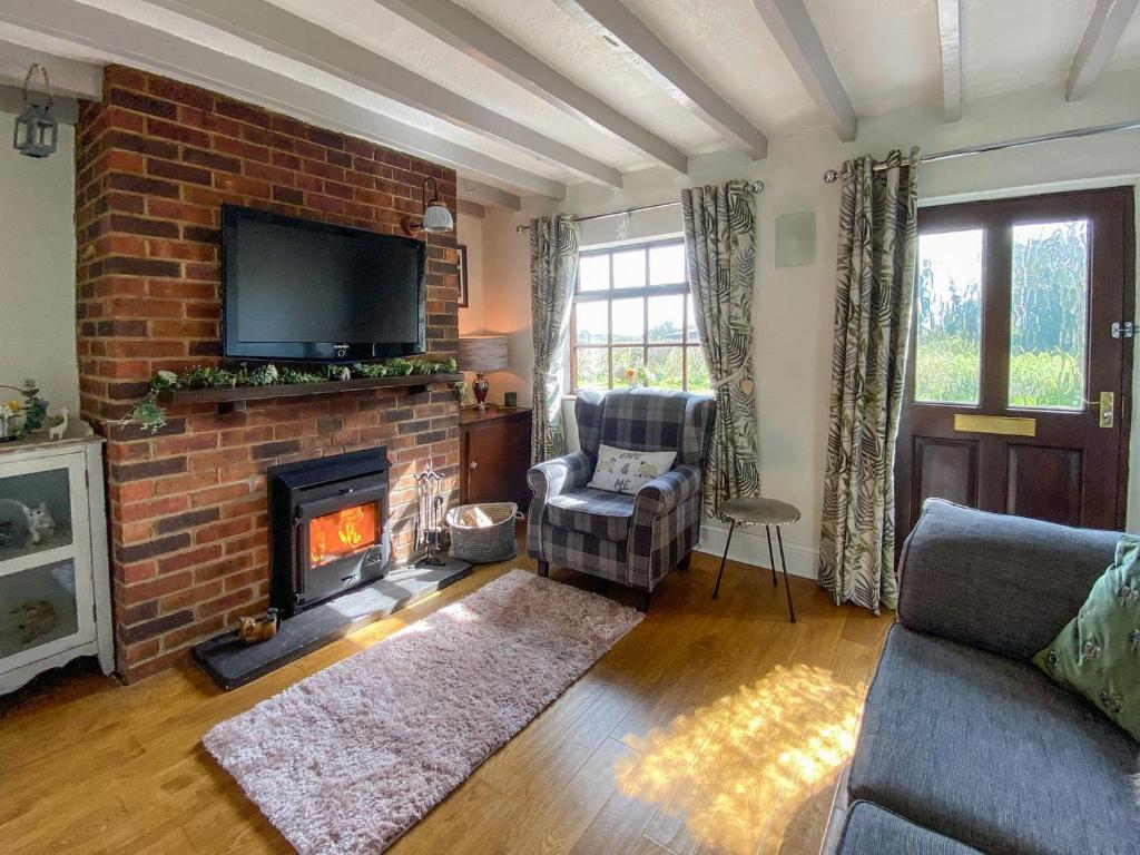 a living room with a brick fireplace and a tv at Wilne Cottage in Shardlow