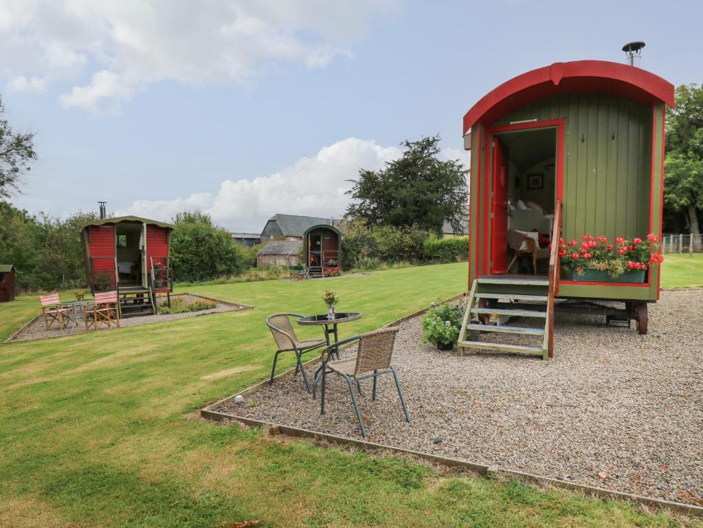 uma pequena casa vermelha e verde com uma mesa e cadeiras em Sweet Briar Shepherds Hut em Brecon