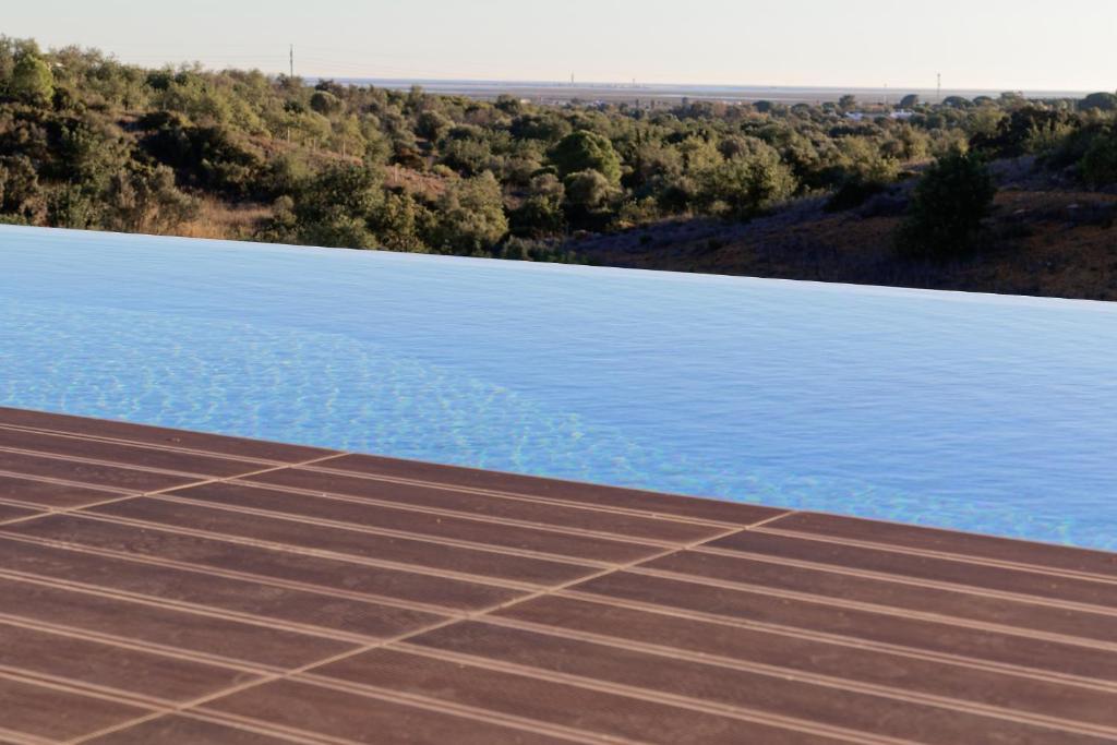 a view of a swimming pool with a field and trees at Tower Villa w Infinity Pool in Olhão