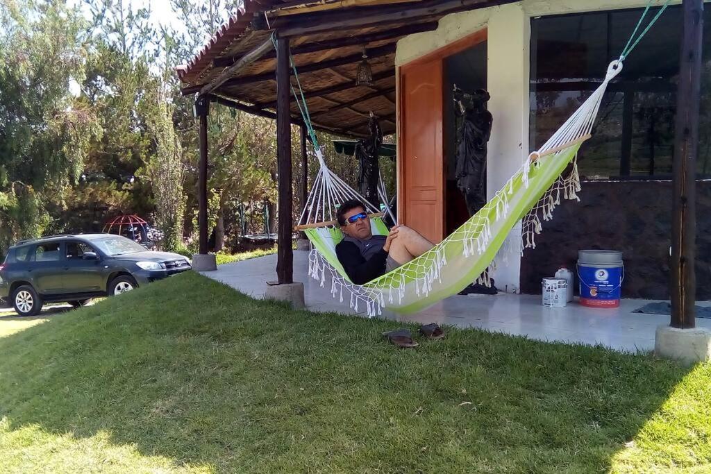 un uomo seduto su un'amaca fuori da una casa di Casa de Campo Arequipa - Disfruta de la naturaleza ad Arequipa