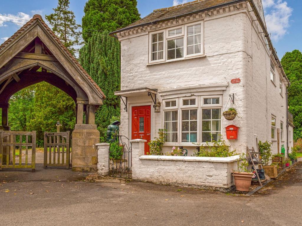 uma casa branca com uma porta vermelha e um portão em The Old Post Office em Aston Cantlow