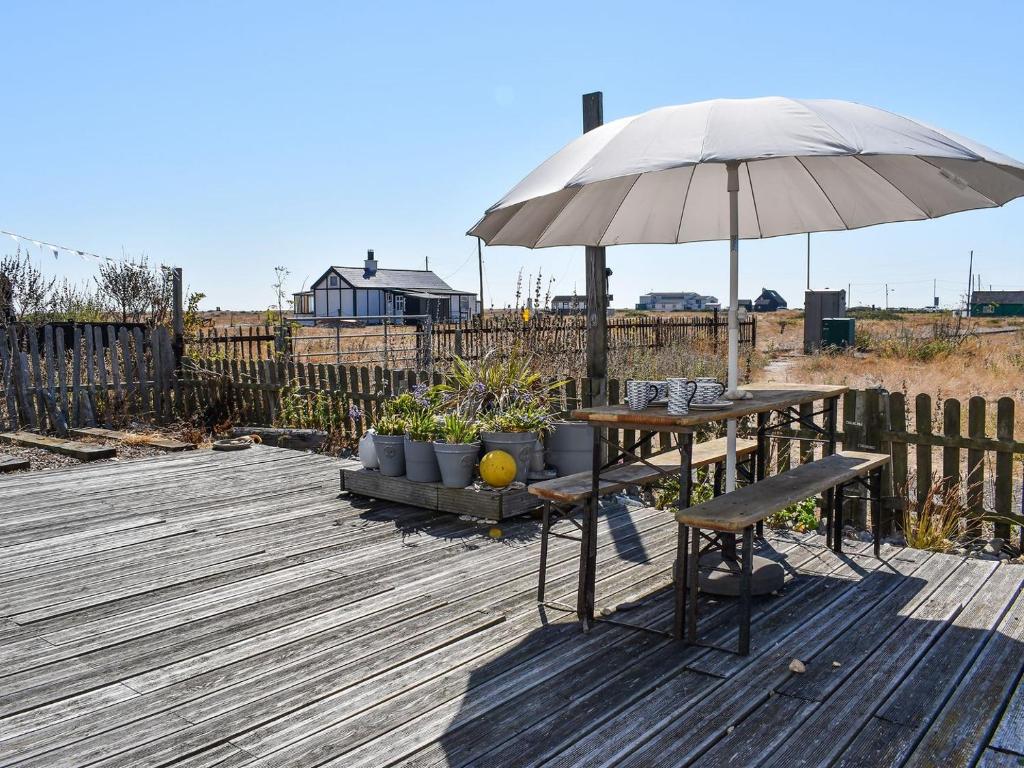 eine Holzterrasse mit einem Tisch und einem Sonnenschirm in der Unterkunft Gull House in Dungeness